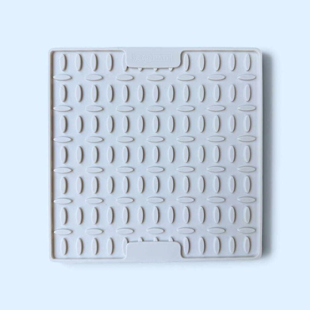 A square white silicone or rubber dish drying rack mat trivet with a textured grid pattern and two integrated handle slots, shown on a light blue background.