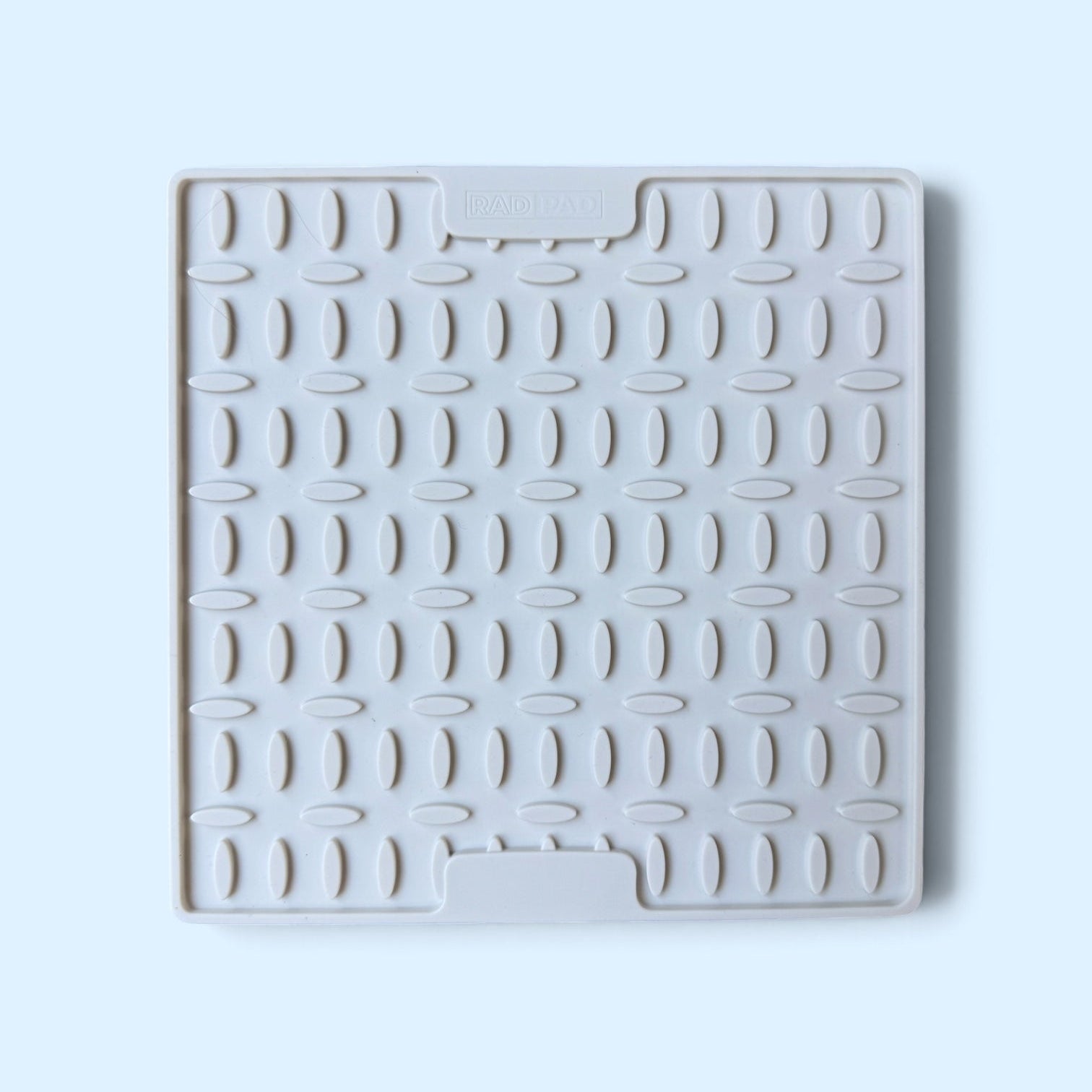 A square white silicone or rubber dish drying rack mat trivet with a textured grid pattern and two integrated handle slots, shown on a light blue background.