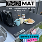 A dark gray RAD MAT camper bench mat shown installed on a camper kitchen counter, with a coffee machine, mugs, toast, and towels. Text overlays read 'RAD MAT', 'YOUR CAMPER BENCH WILL THANK YOU.